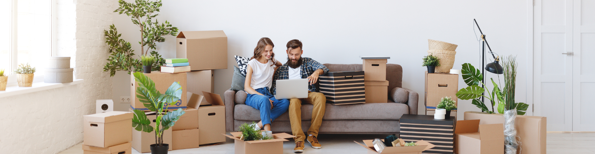 A man and a woman sitting on a couch with boxes and a laptop.