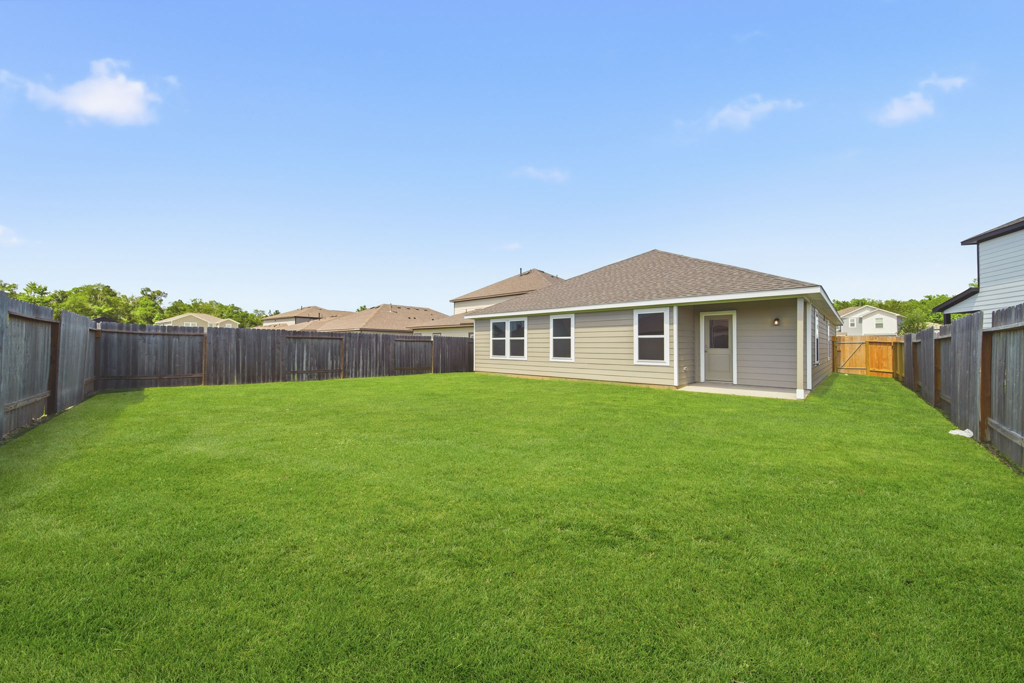 A grassy yard with a fence and a house in the background.
