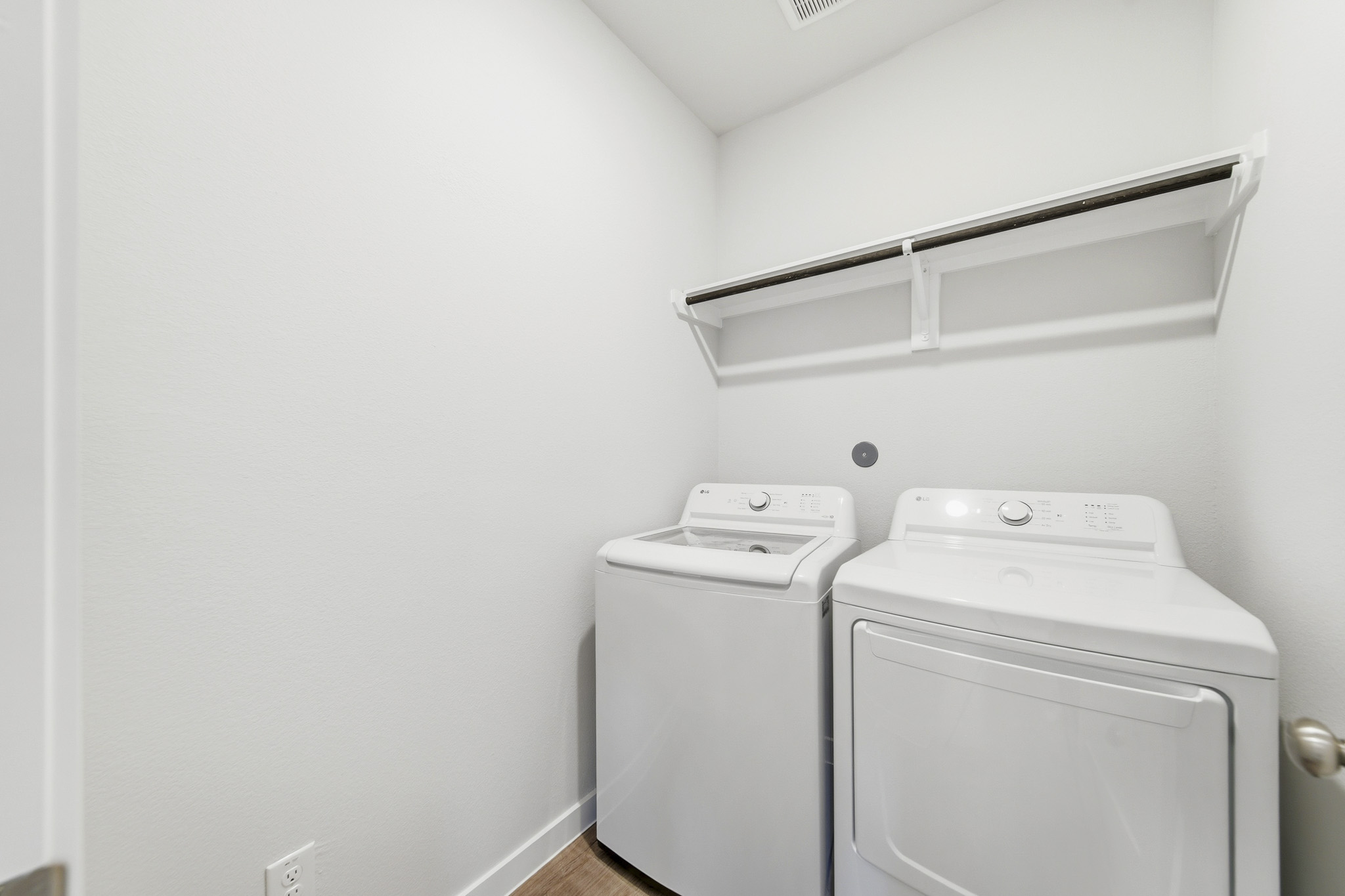 A white laundry room with a white wall and a white shelf.
