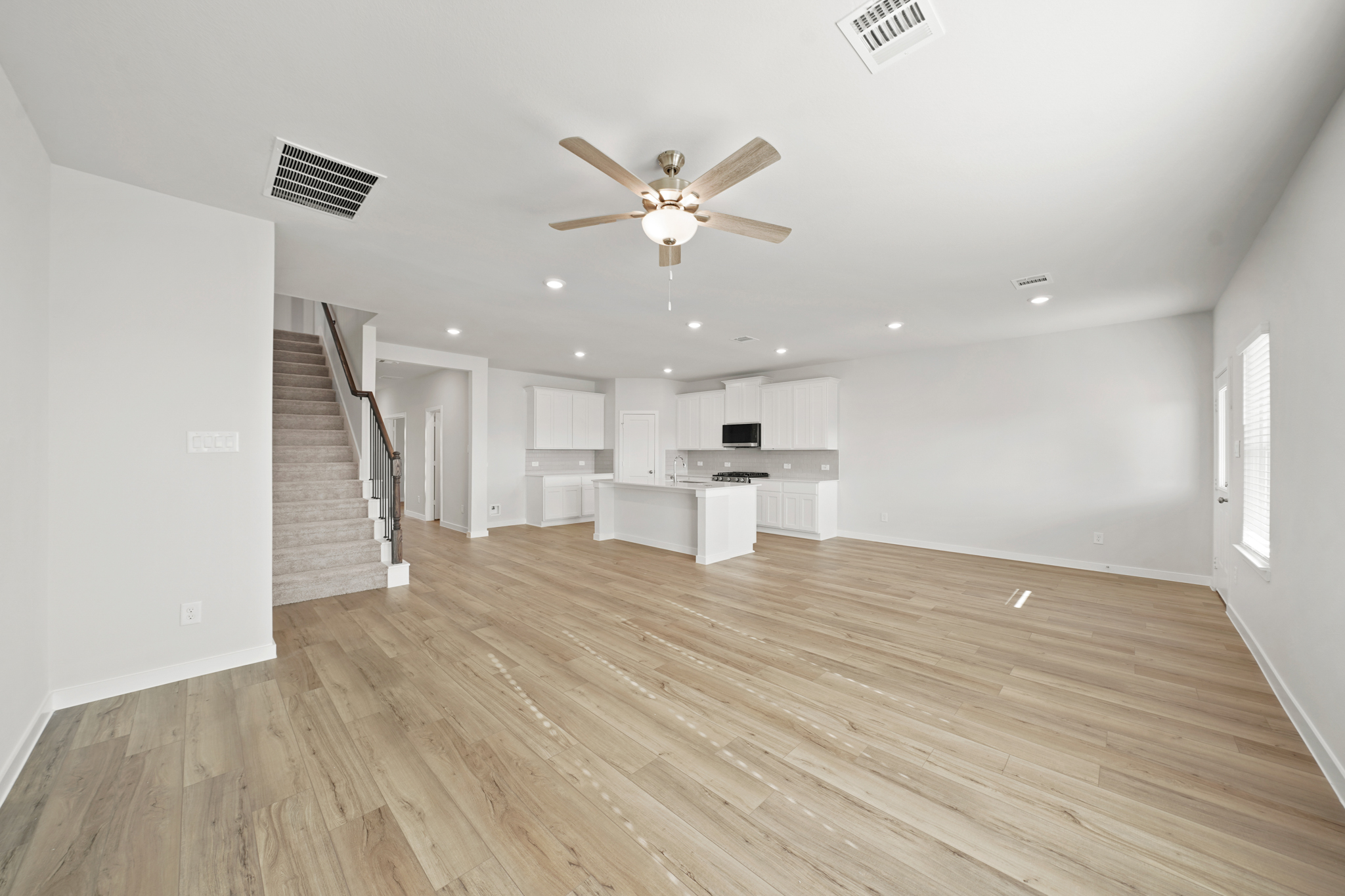 A large empty room with a wood floor and a ceiling fan.