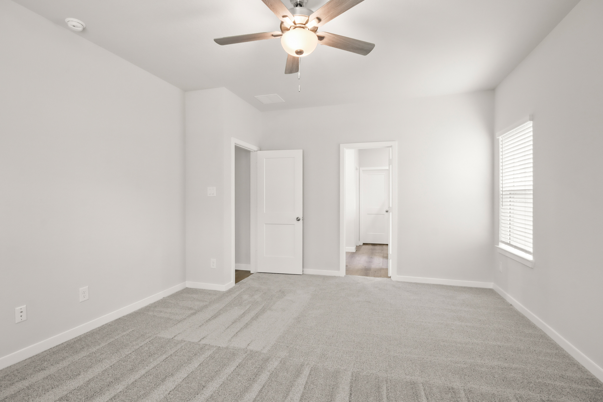 A room with a ceiling fan and white walls.